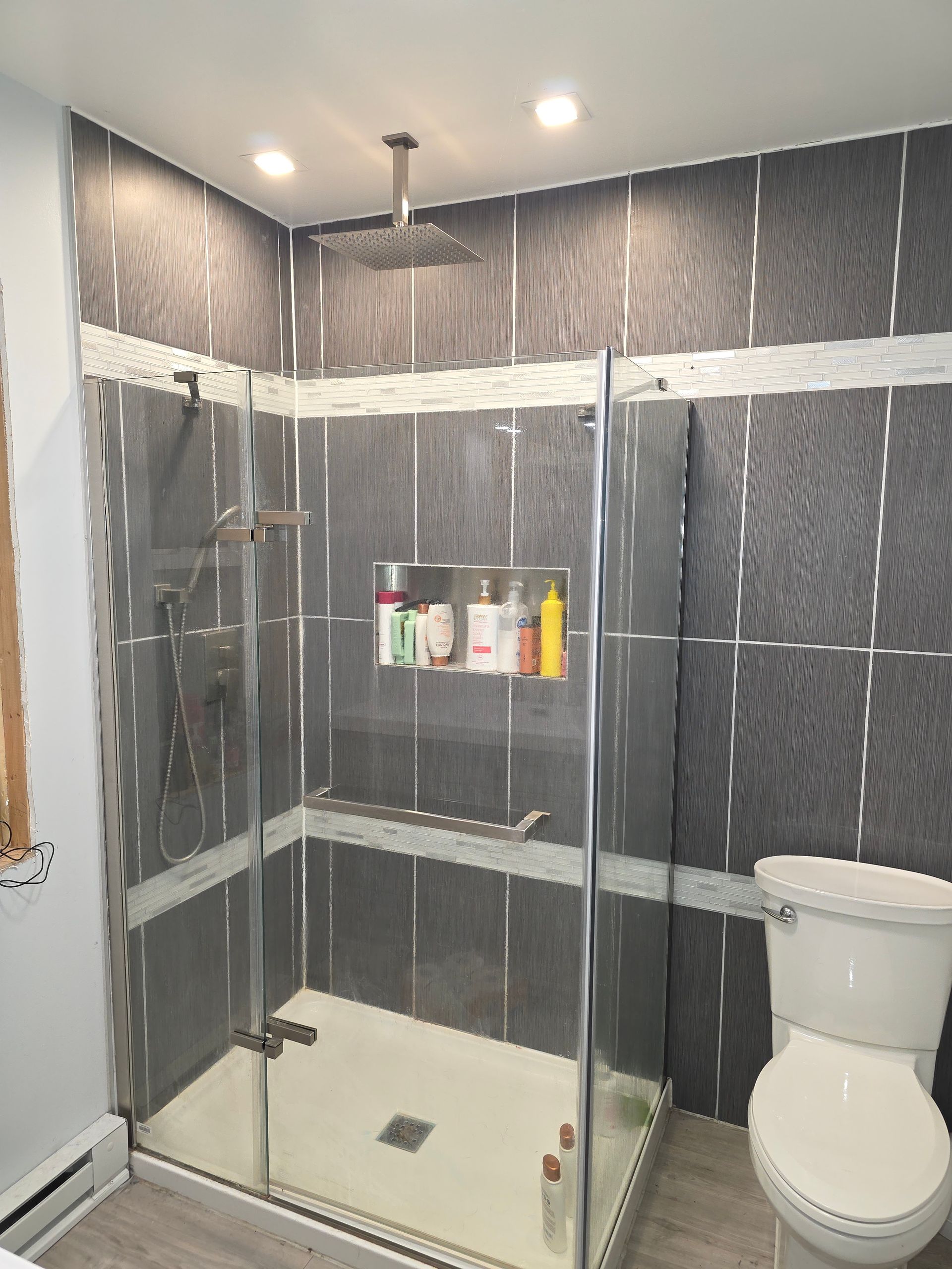 Modern bathroom with a glass shower, gray tiled walls, and a white toilet.
