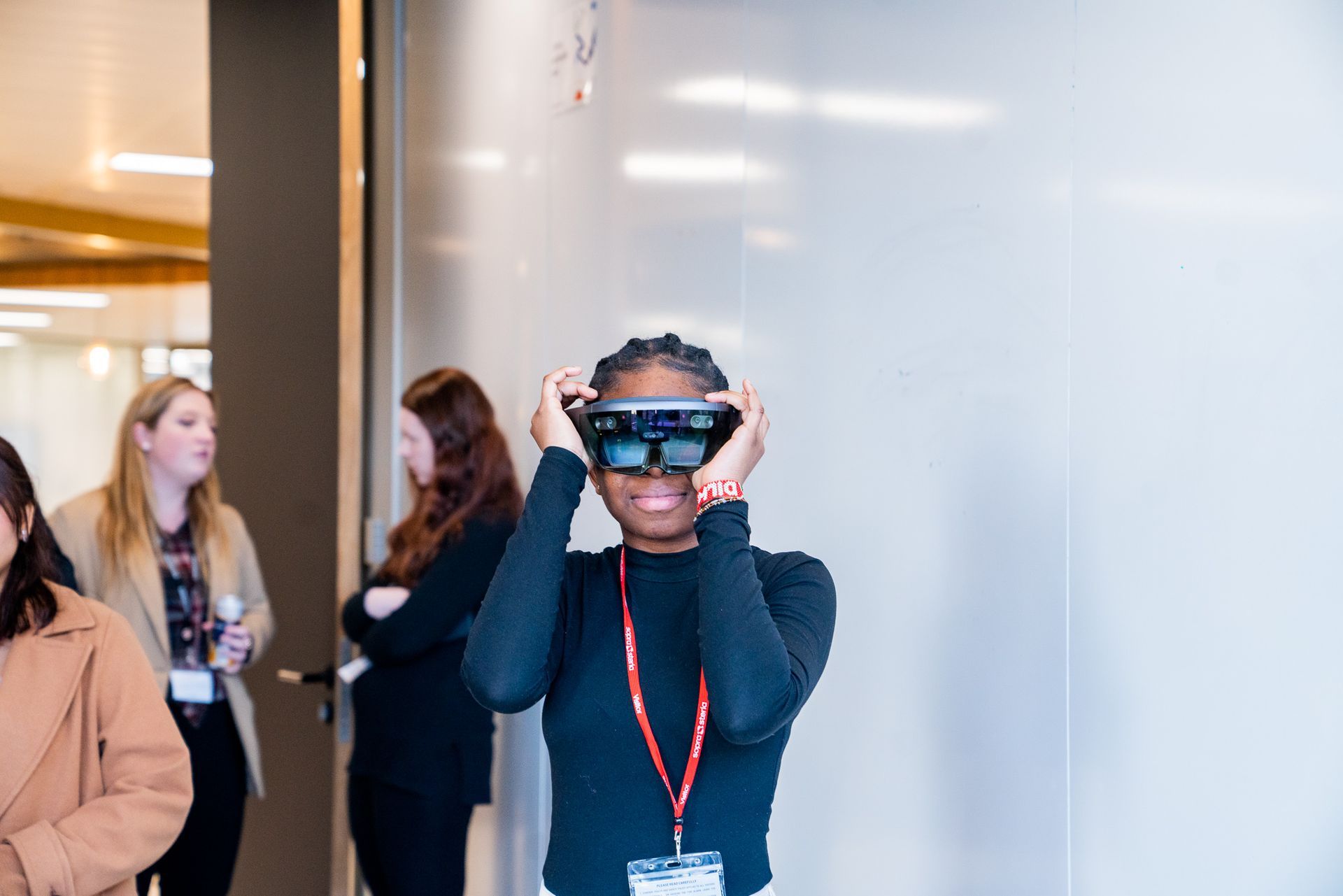 Person wearing a VR headset and holding it in place in a bright indoor lobby.