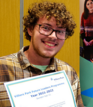 Smiling person holding a certificate, wearing glasses and a plaid shirt, standing indoors.