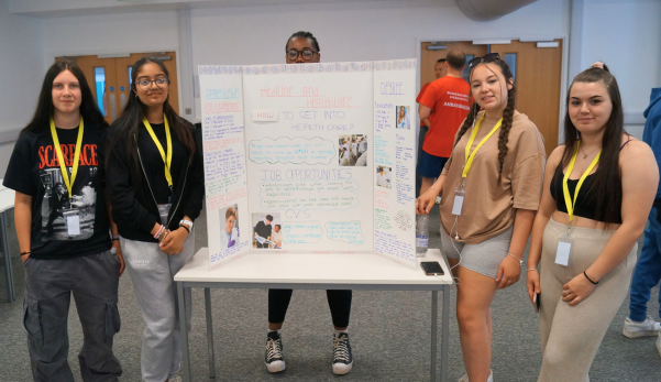 Five people posing around a white presentation board at a conference booth.
