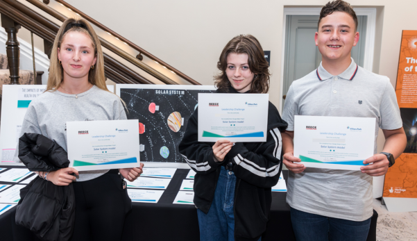 Three people holding certificates at a display table indoors