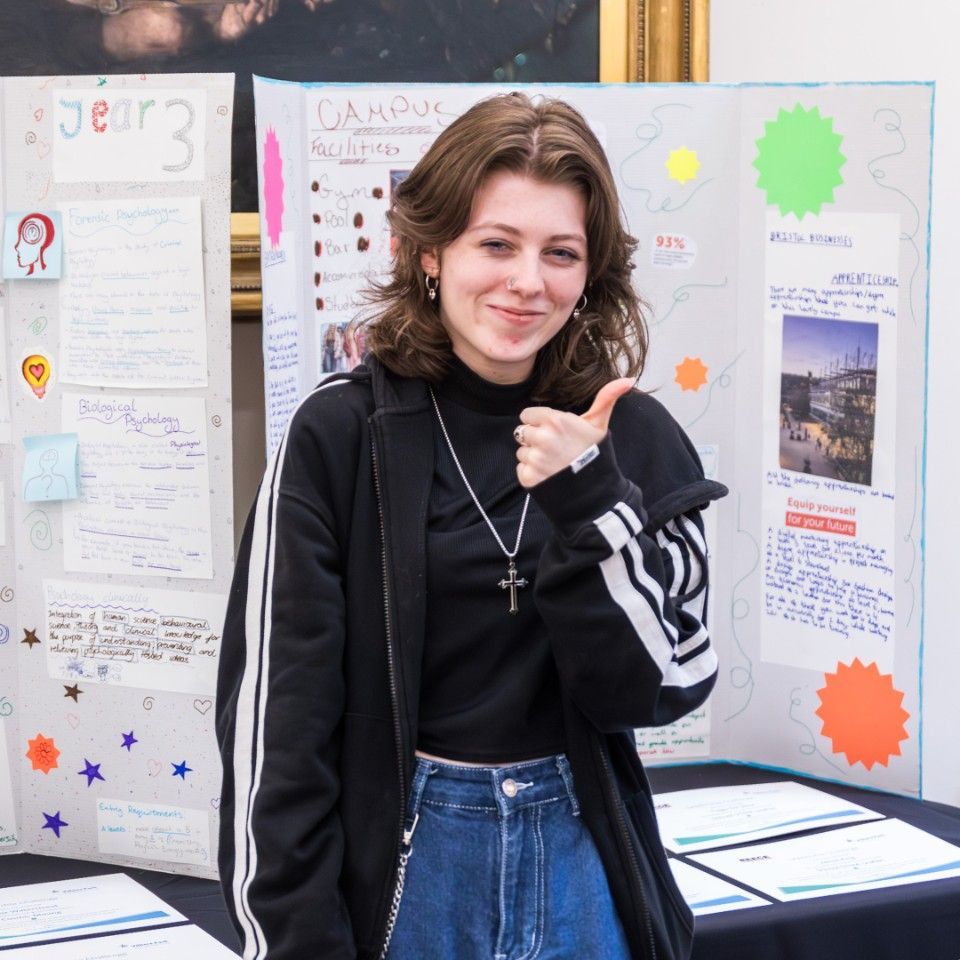 Person smiling and giving a thumbs-up in front of colorful display boards at a school event