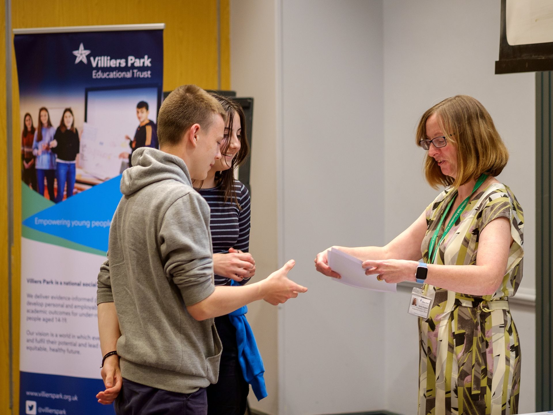 People exchanging papers at a Villiers Park Educational Trust event booth.