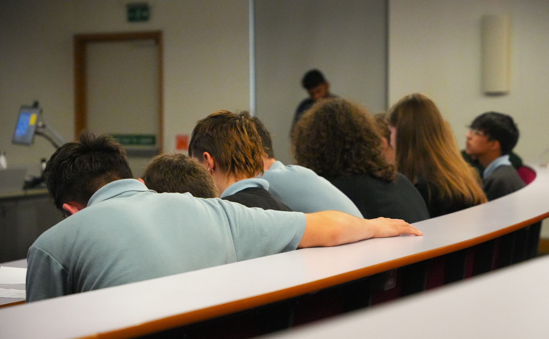 People seated in a lecture hall, seen from behind, listening to a presentation.