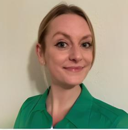Person in a green top smiling against a plain light-colored wall