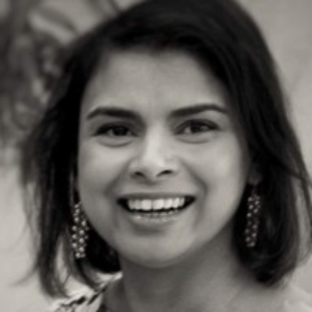 Smiling person with shoulder-length dark hair wearing dangling earrings, in a black-and-white portrait