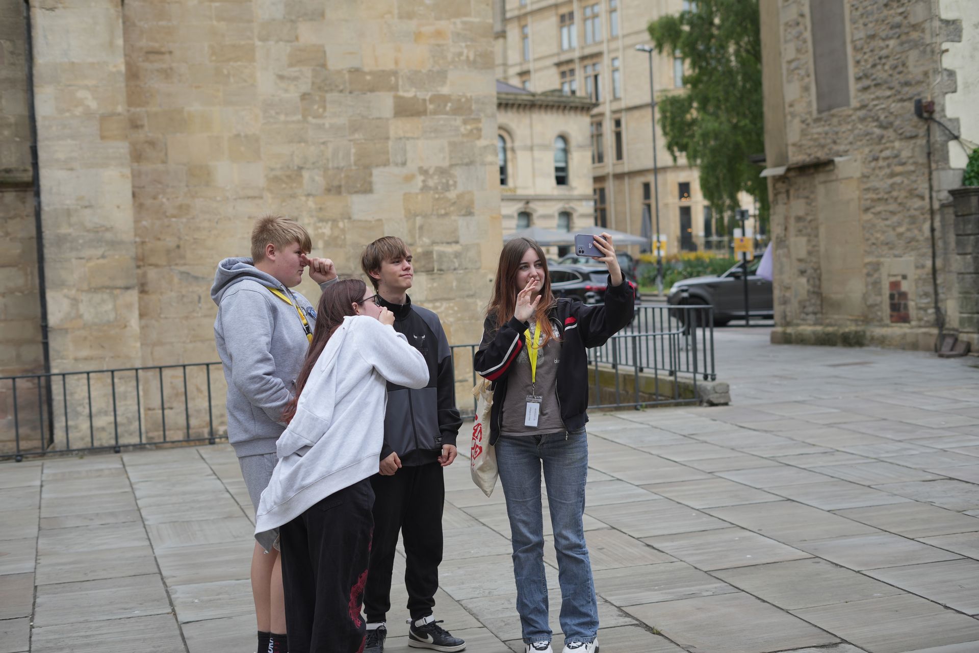 Four people standing outside a stone building, one holding a camera on a city street