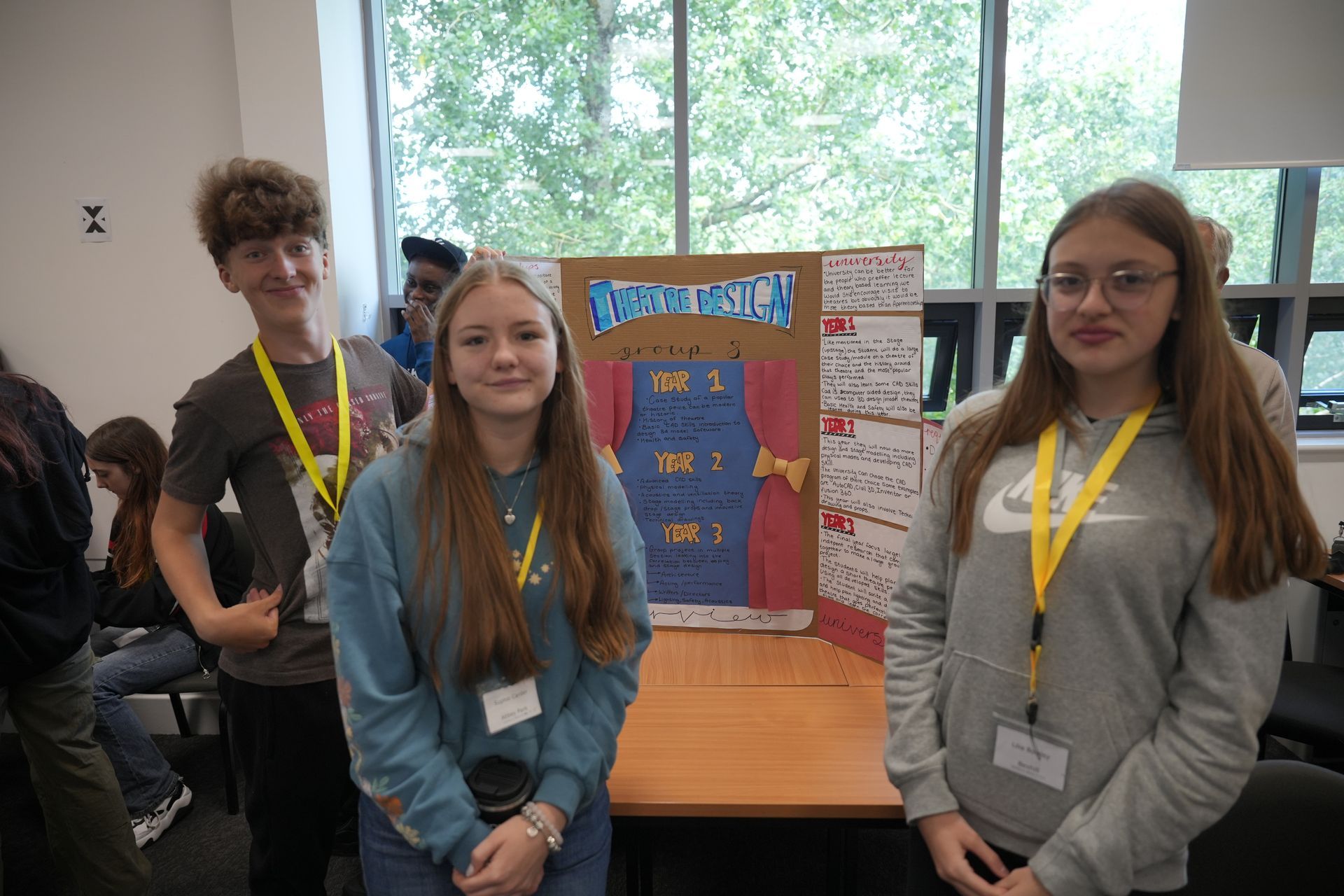 Three students standing beside a science fair project display in a bright room