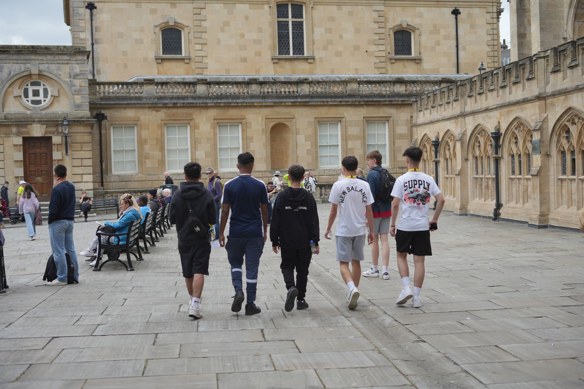 People walking across a stone courtyard beside an old building and arcade.
