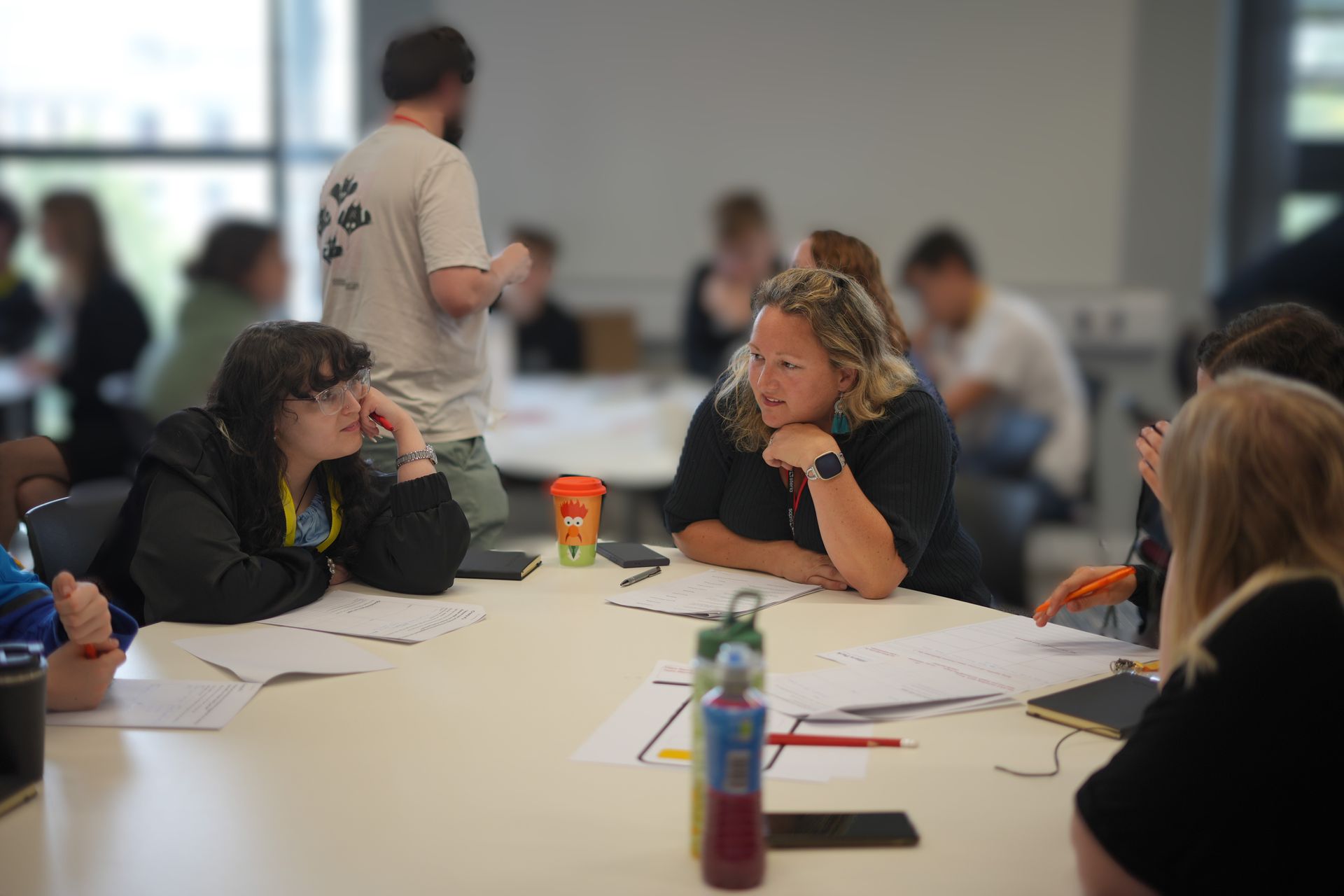 People seated around a table in a meeting room, discussing papers and notes.