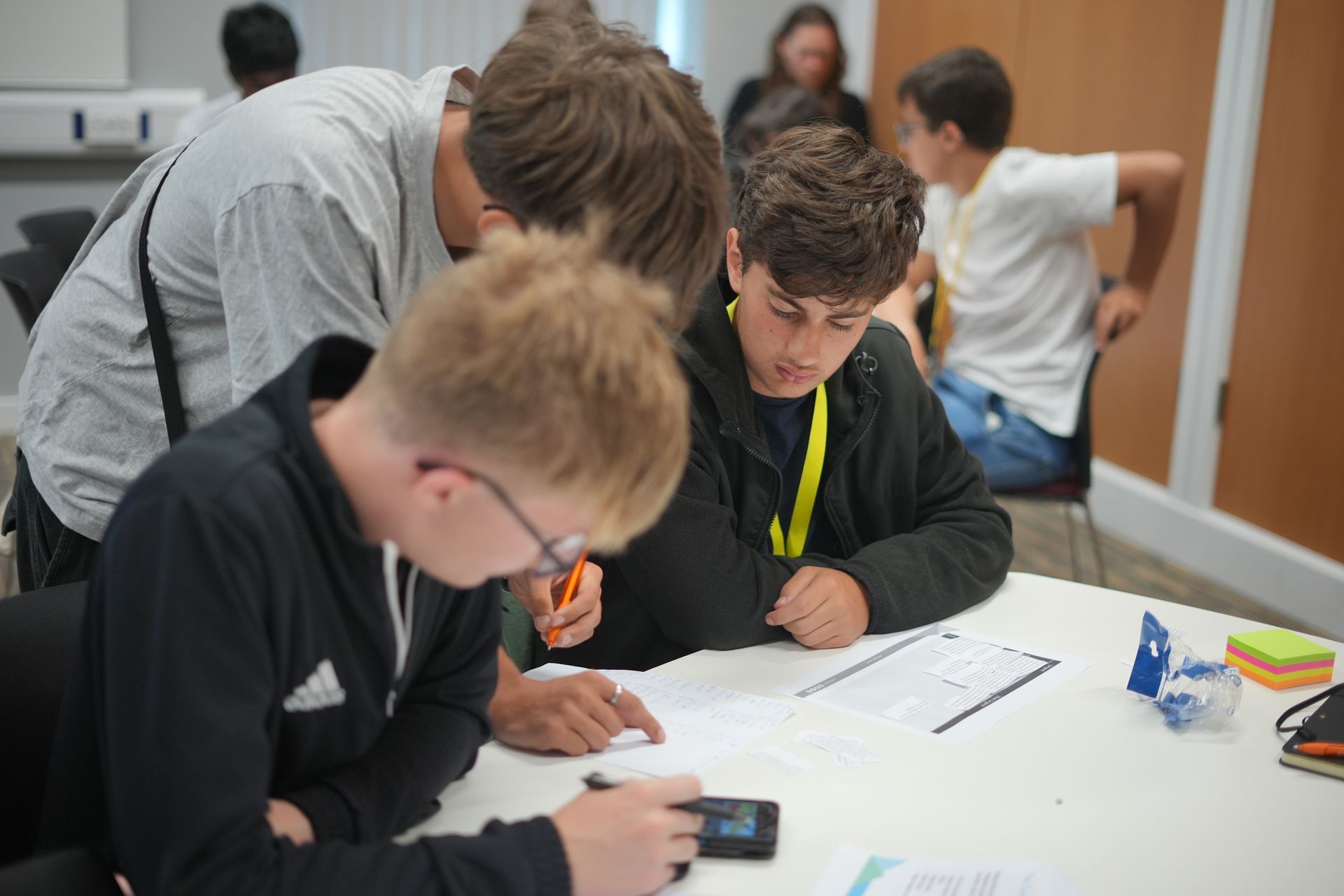 Students collaborating at a table, writing on paper in a classroom setting