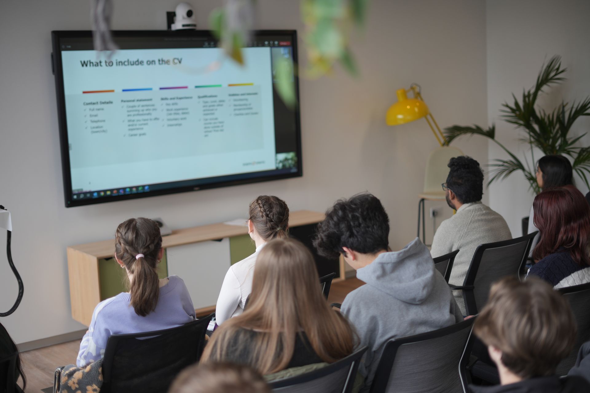 People seated in a conference room watching a presentation on a wall-mounted screen