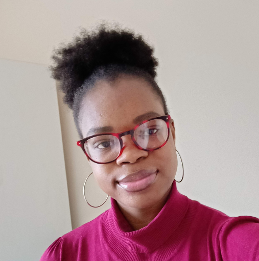 Portrait of a person wearing red glasses and a magenta top, smiling gently indoors