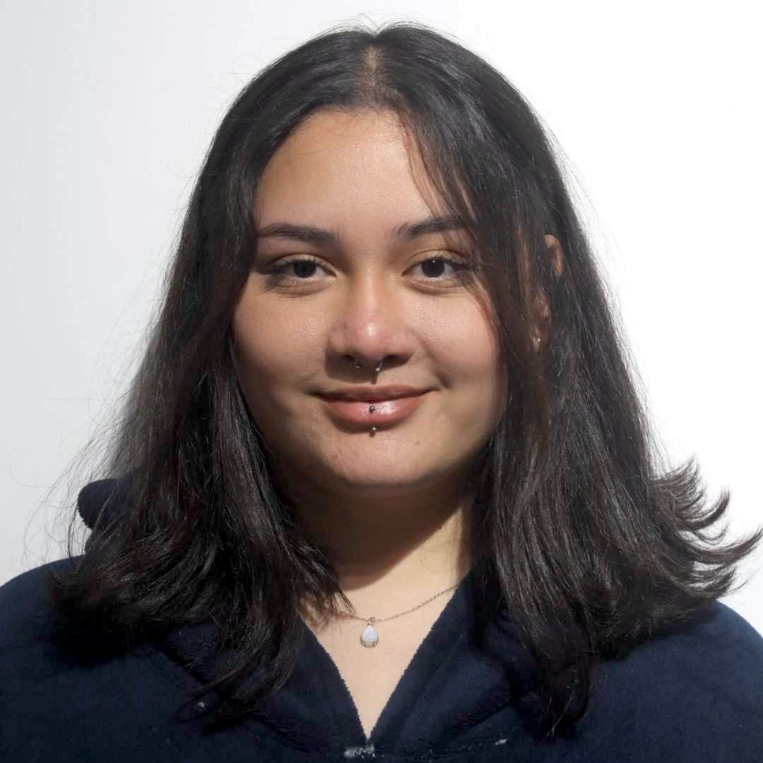 Portrait of a smiling person with shoulder-length dark hair, wearing a navy top against a white background