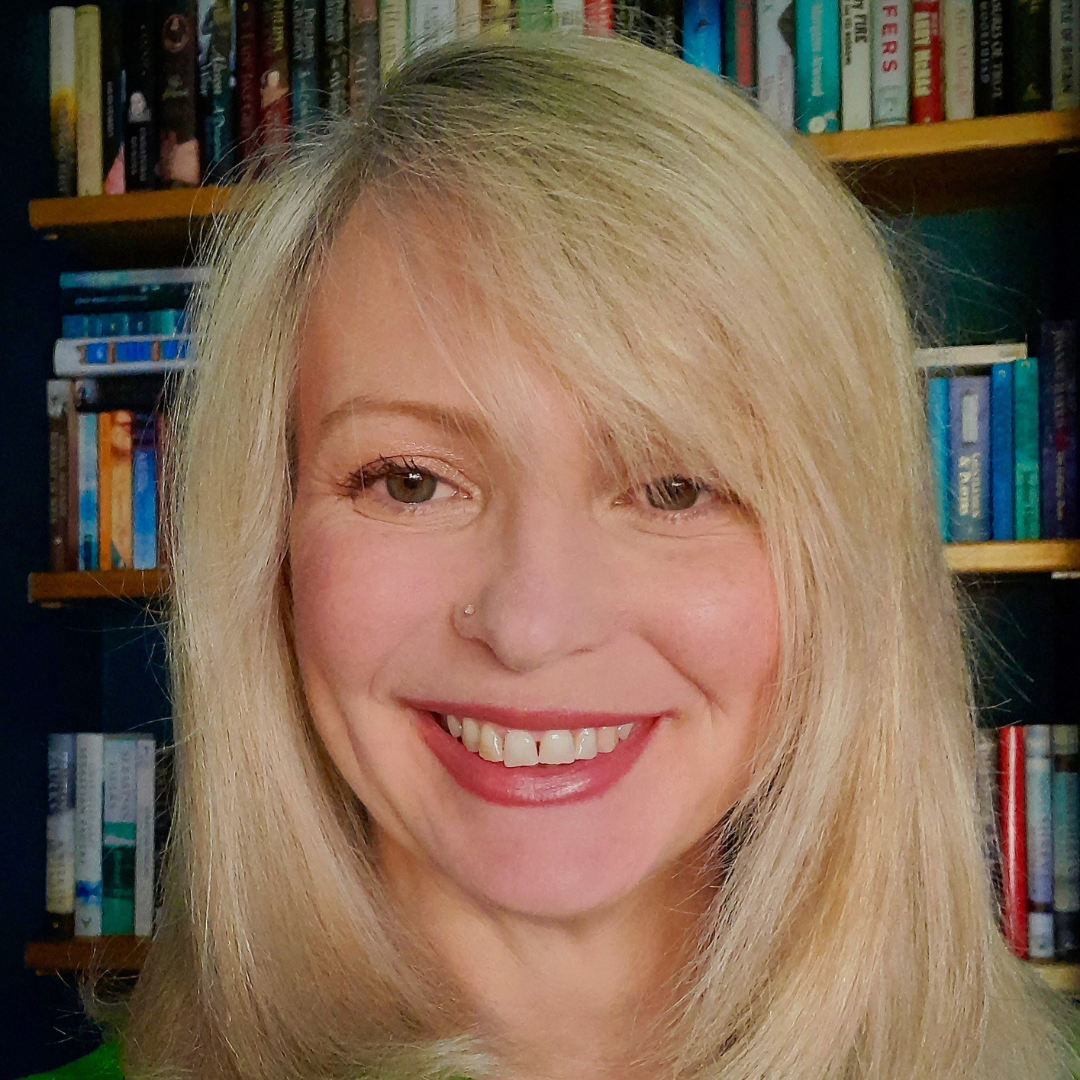 Smiling blonde woman in front of a bookshelf, with a nose ring and red lipstick
