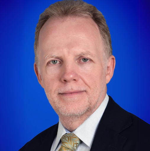 Professional headshot of a man in a dark suit and tie against a blue background