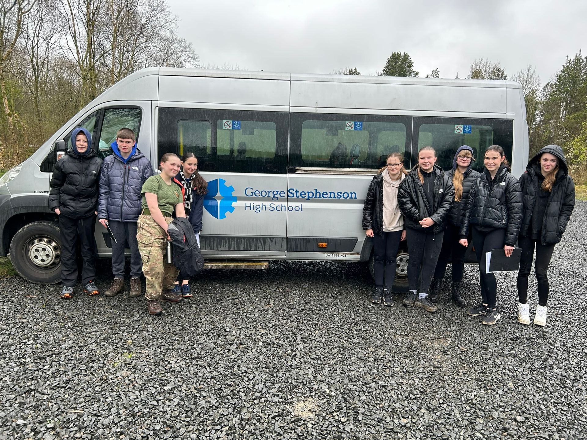 Group of people standing beside a white van in a gravel lot on a cloudy day