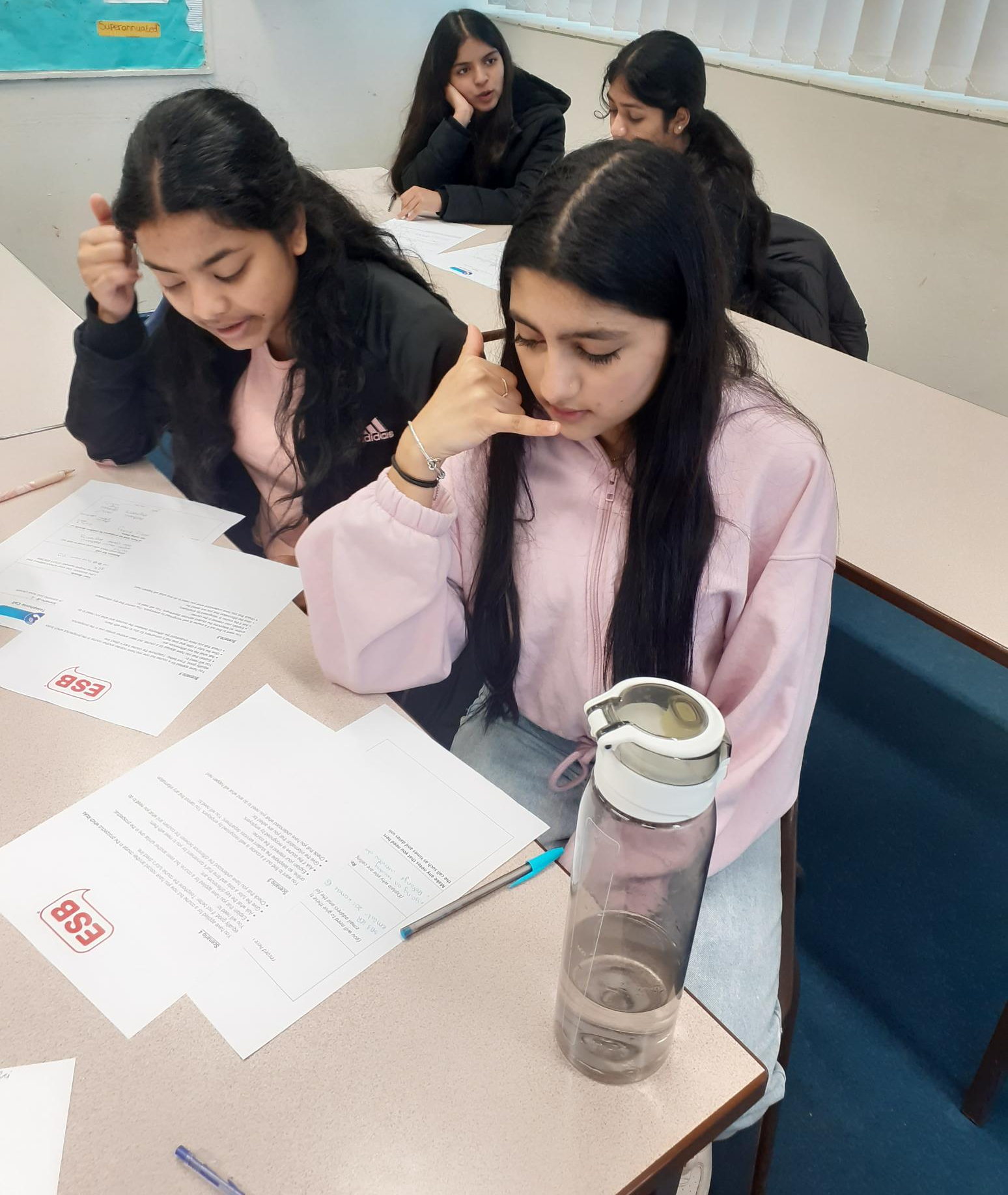 Students seated at desks in a classroom, reading papers and working quietly