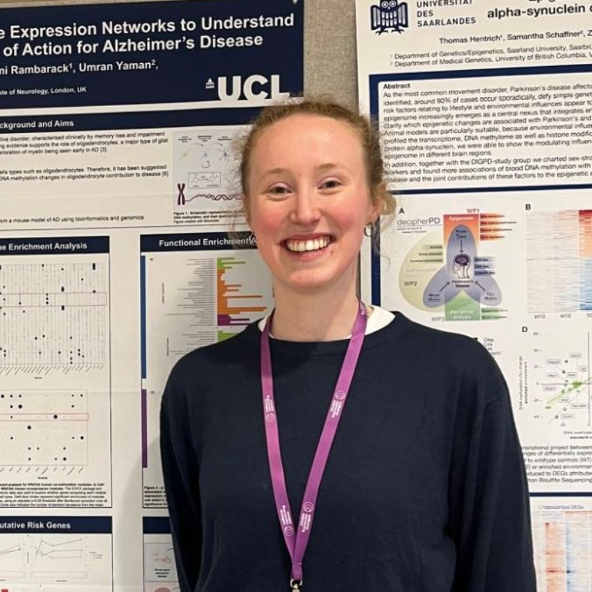 Smiling person wearing a purple lanyard stands in front of an Alzheimer’s research poster at a conference