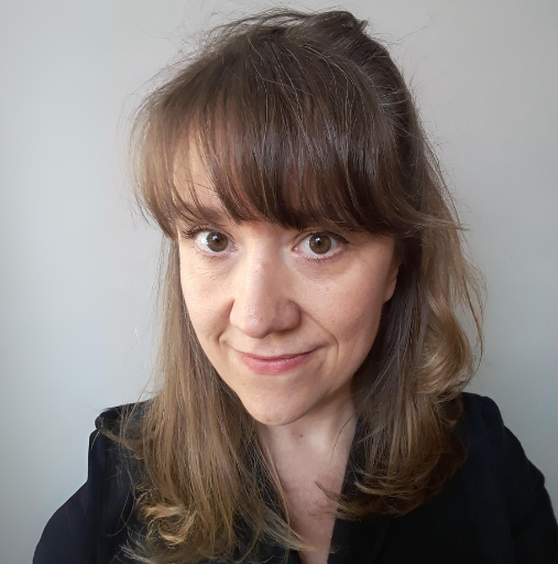 Portrait of a smiling woman with brown hair and bangs, wearing a black top against a plain light background