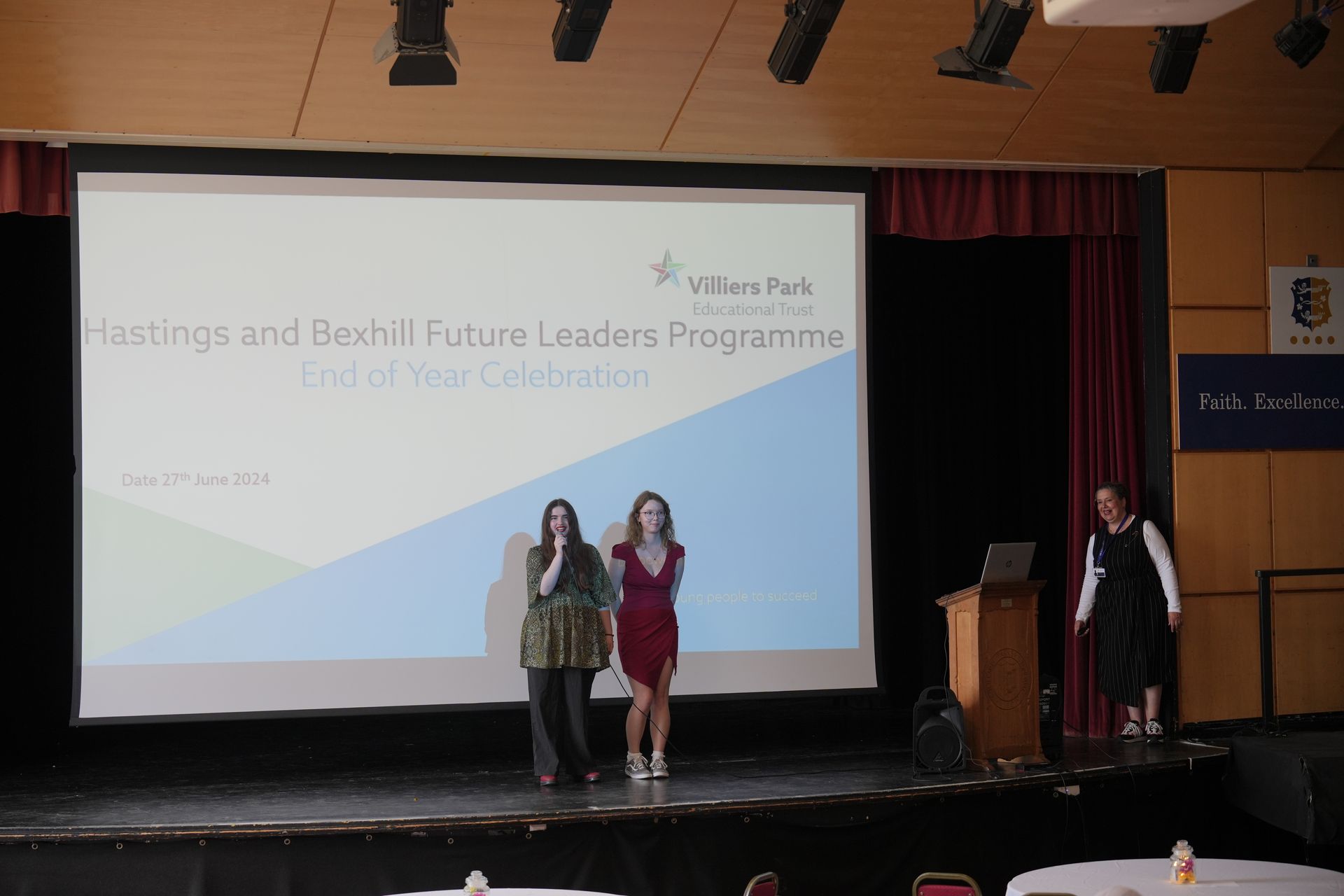 Three people on a stage at a leadership program, with a presentation screen and podium in the background.