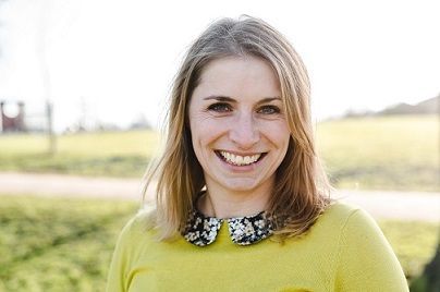 Smiling woman in a yellow sweater standing outdoors in a sunny field
