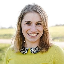 Smiling woman in a lime green sweater with a patterned collar, standing outdoors in a sunny field