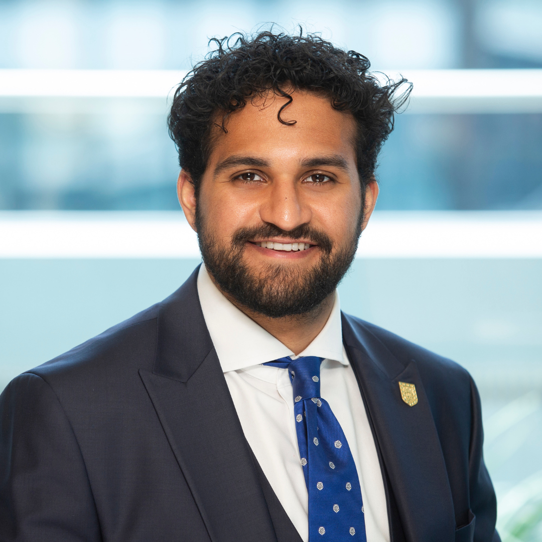 Smiling man in a navy suit and blue tie against a bright office-style background