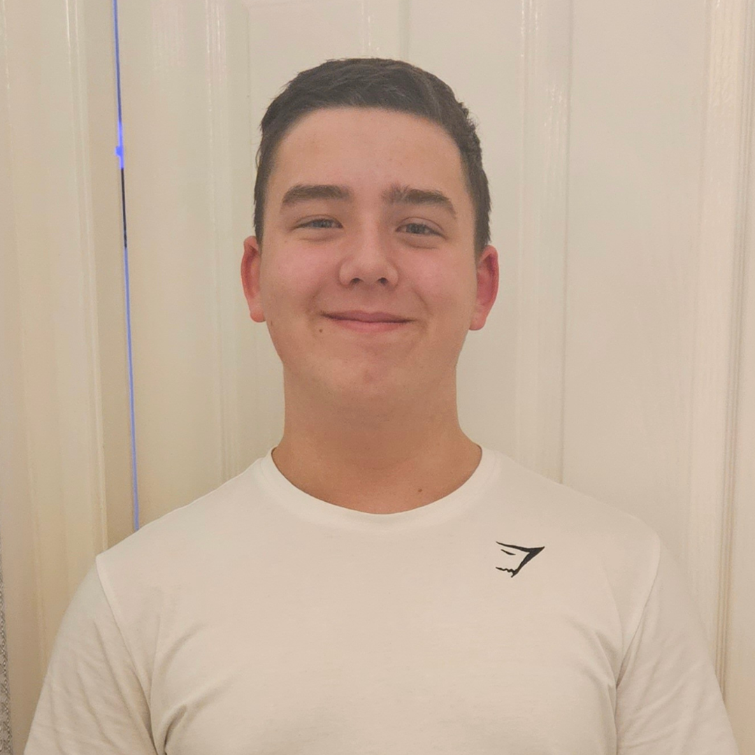 Smiling person in a white T-shirt standing indoors against a light curtain background