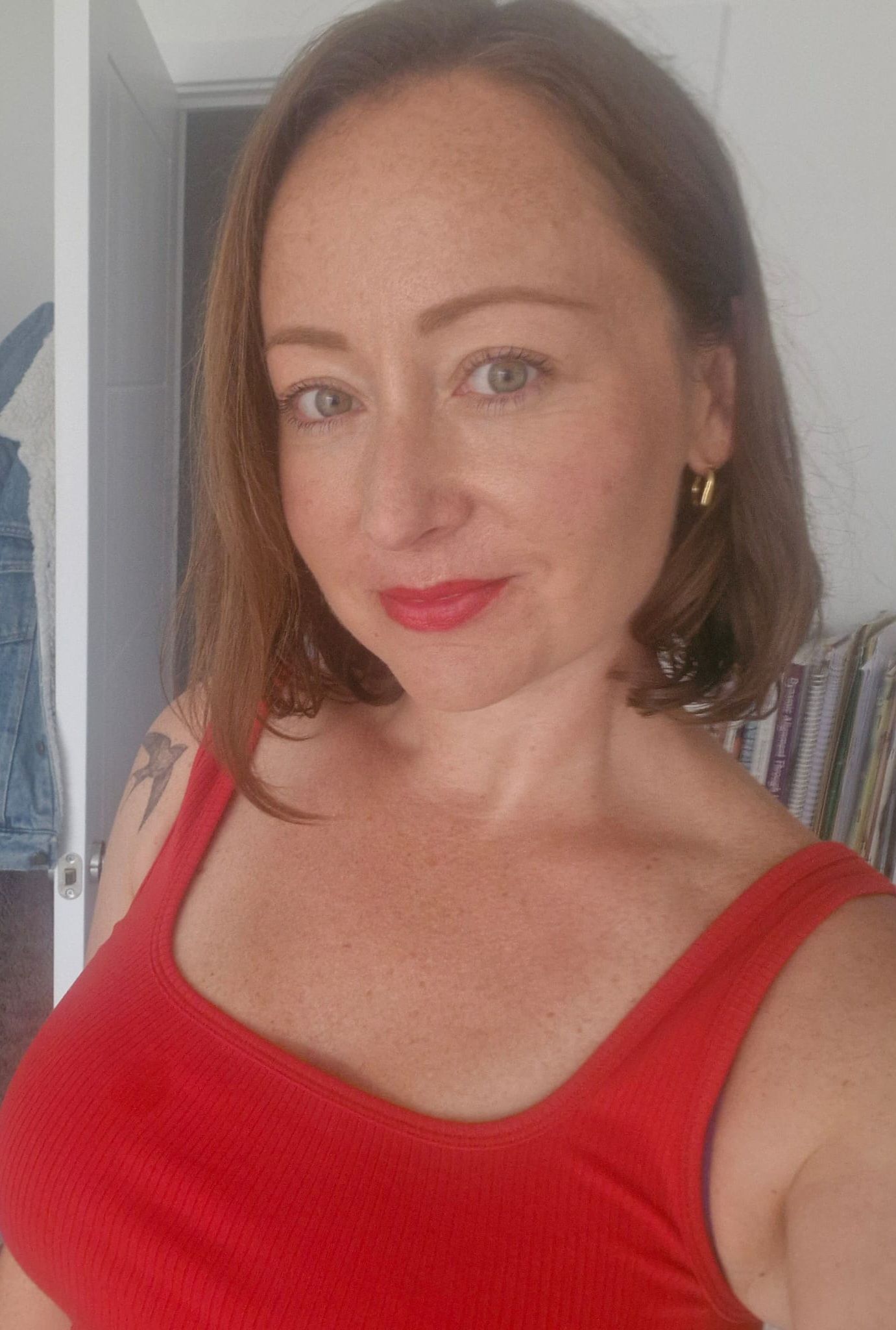 Woman in a red sleeveless top, smiling in a bright indoor setting.