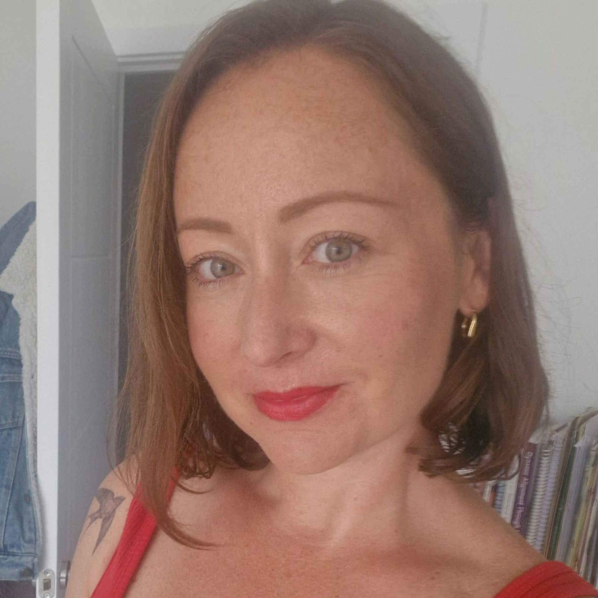 Woman with shoulder-length brown hair and red lipstick, posing indoors in a red top.