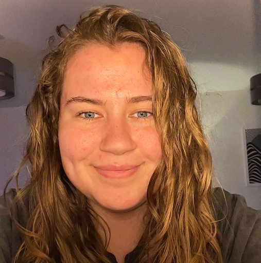 Close-up of a smiling person with wavy hair in soft indoor light