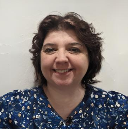 Smiling person in a blue patterned blouse against a plain light background