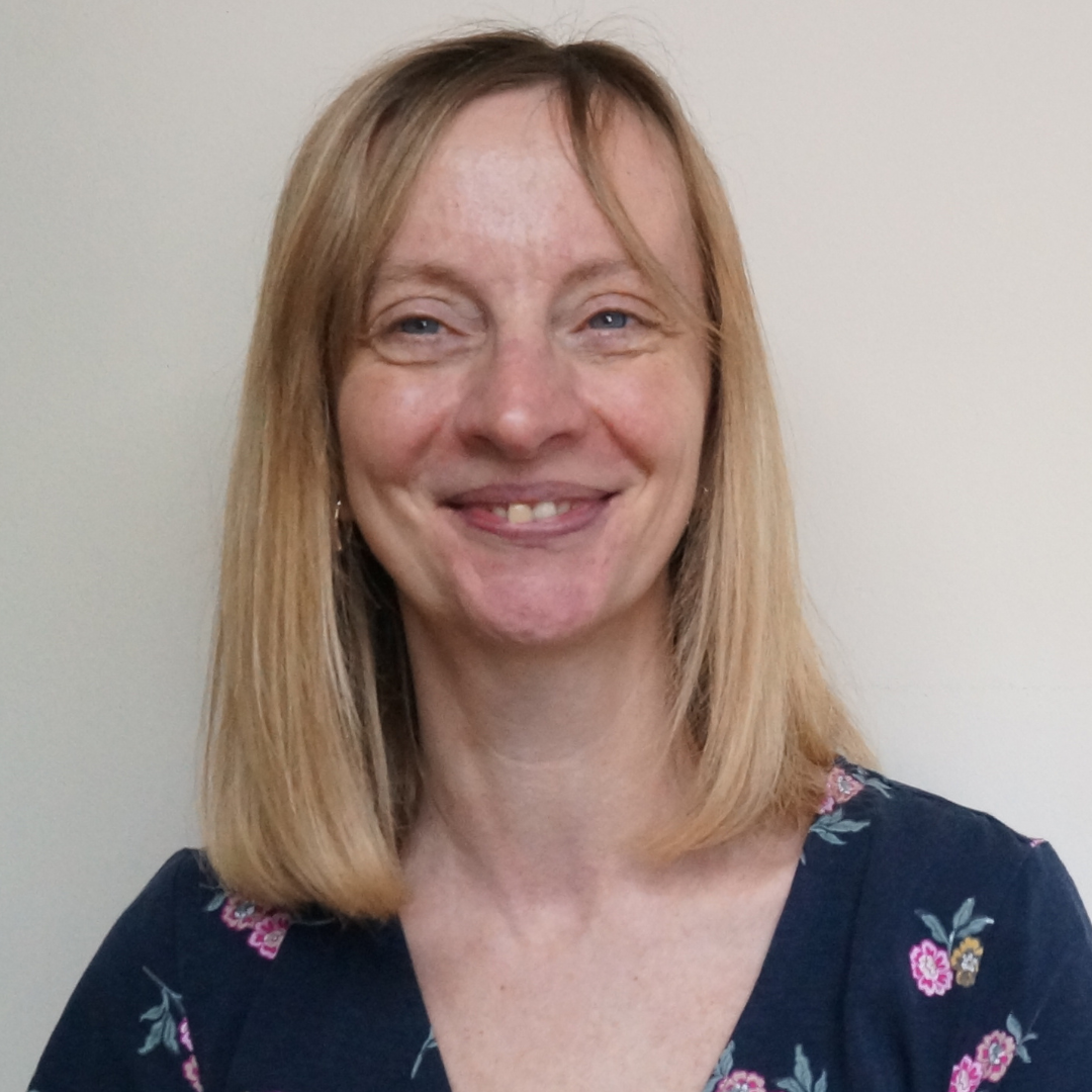 Smiling woman with shoulder-length blond hair in a navy floral top against a plain wall