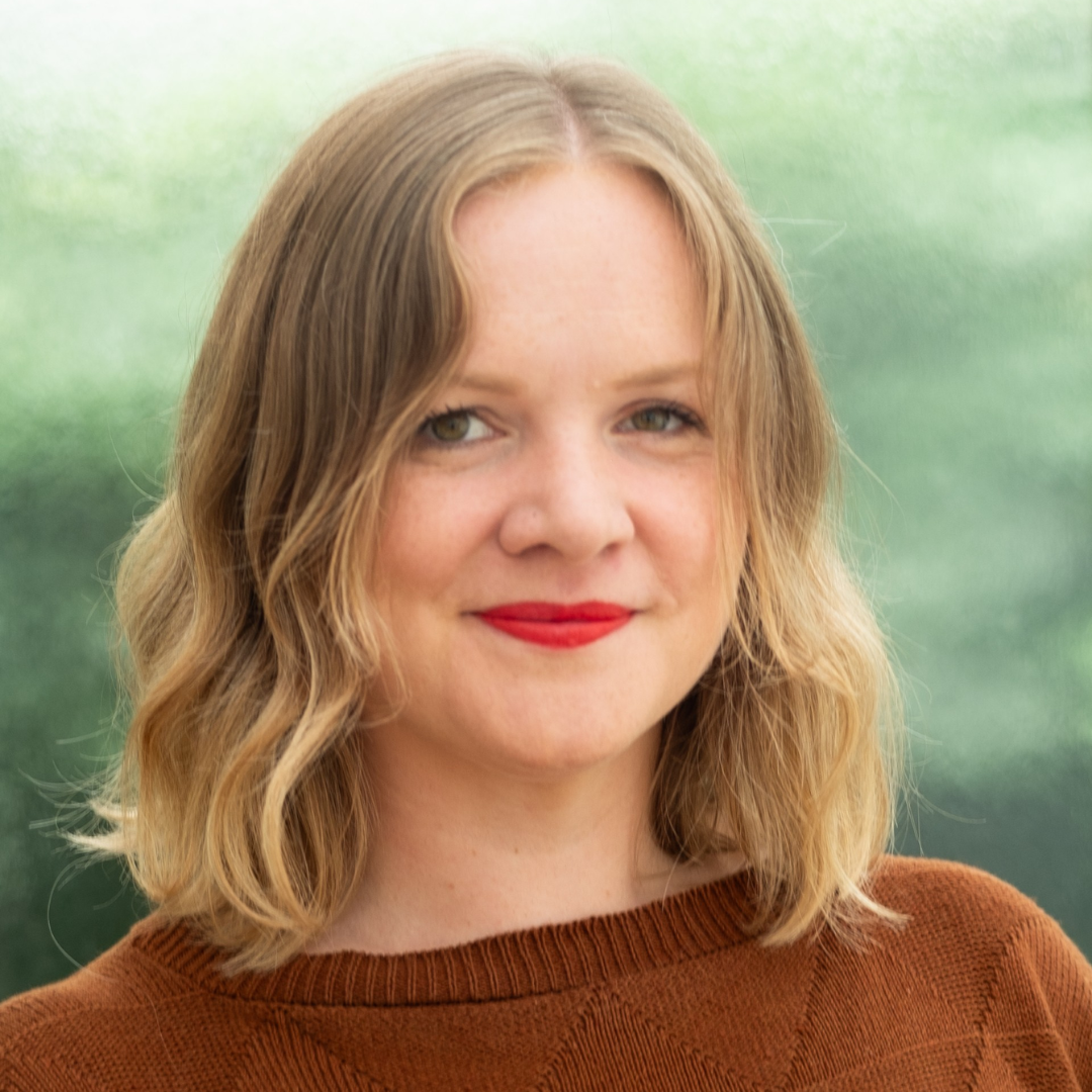 Smiling person with shoulder-length blonde hair and red lipstick against a soft green background