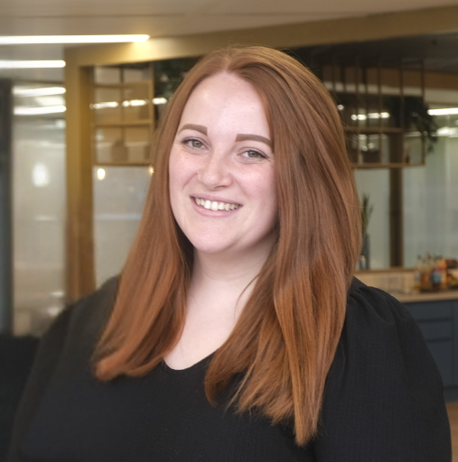 Smiling woman with long red hair in a black top standing in an office lobby