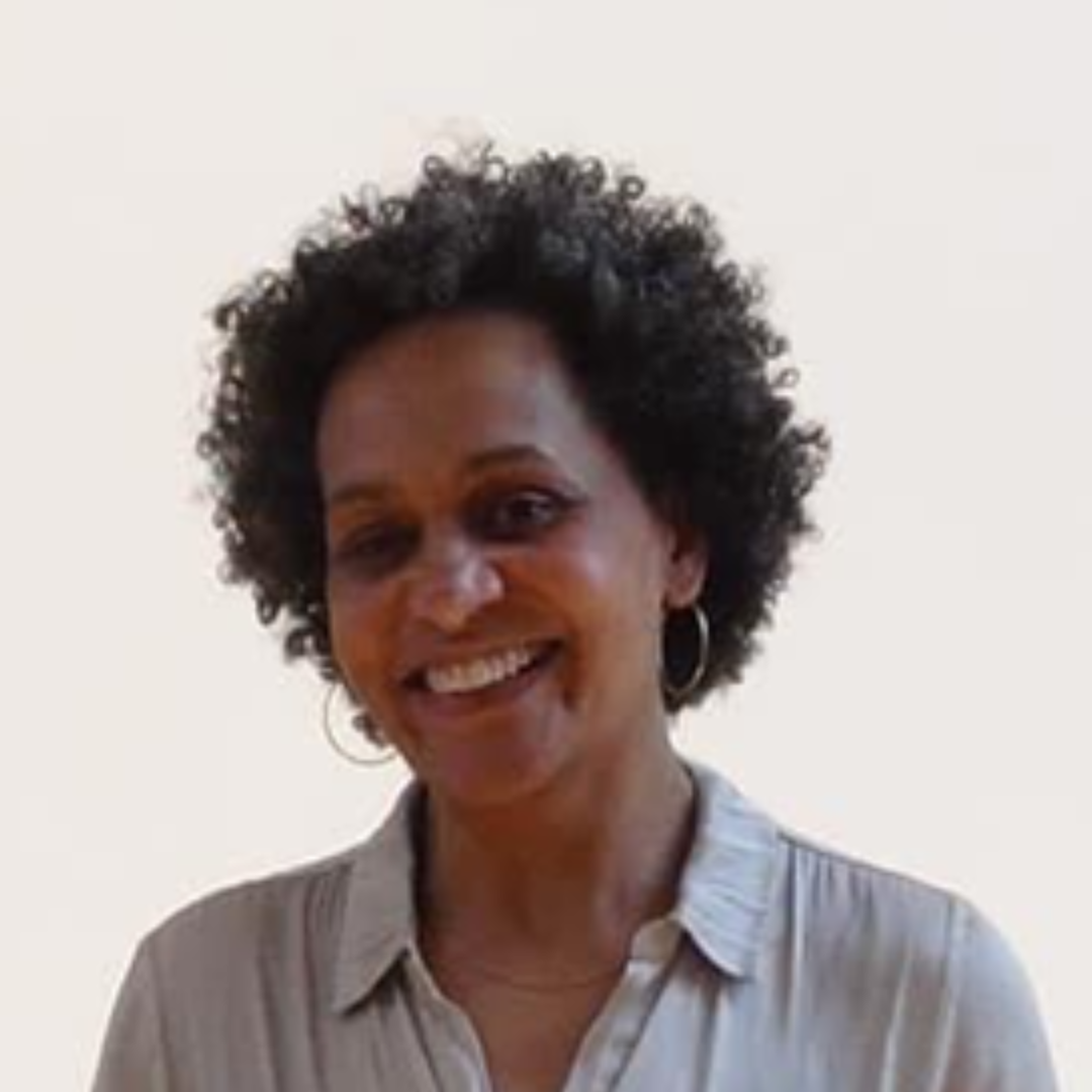 Smiling person with short curly hair in a light gray shirt against a plain white background