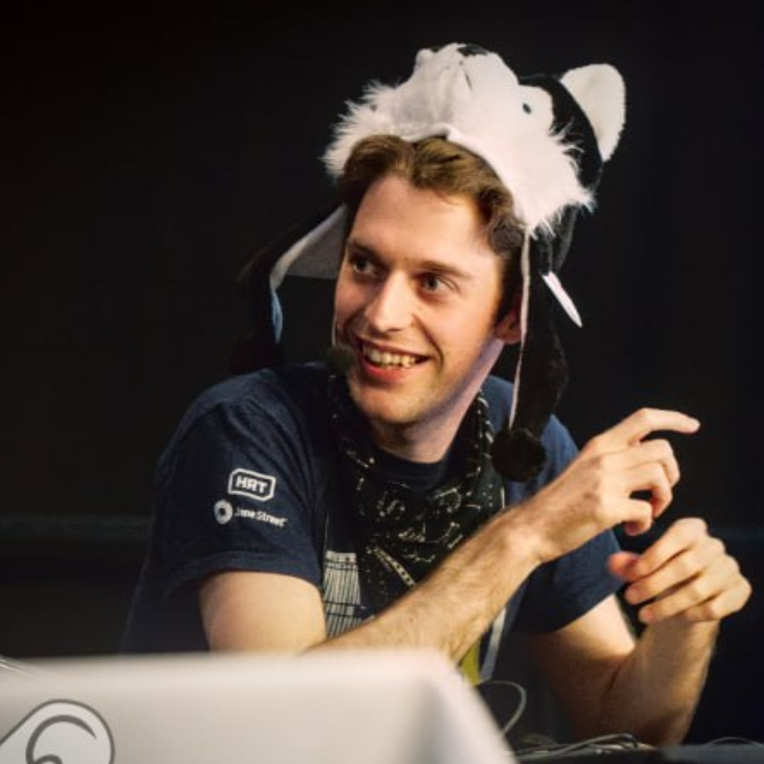 Person smiling at a desk wearing a white-and-black animal hat, in a dark indoor setting