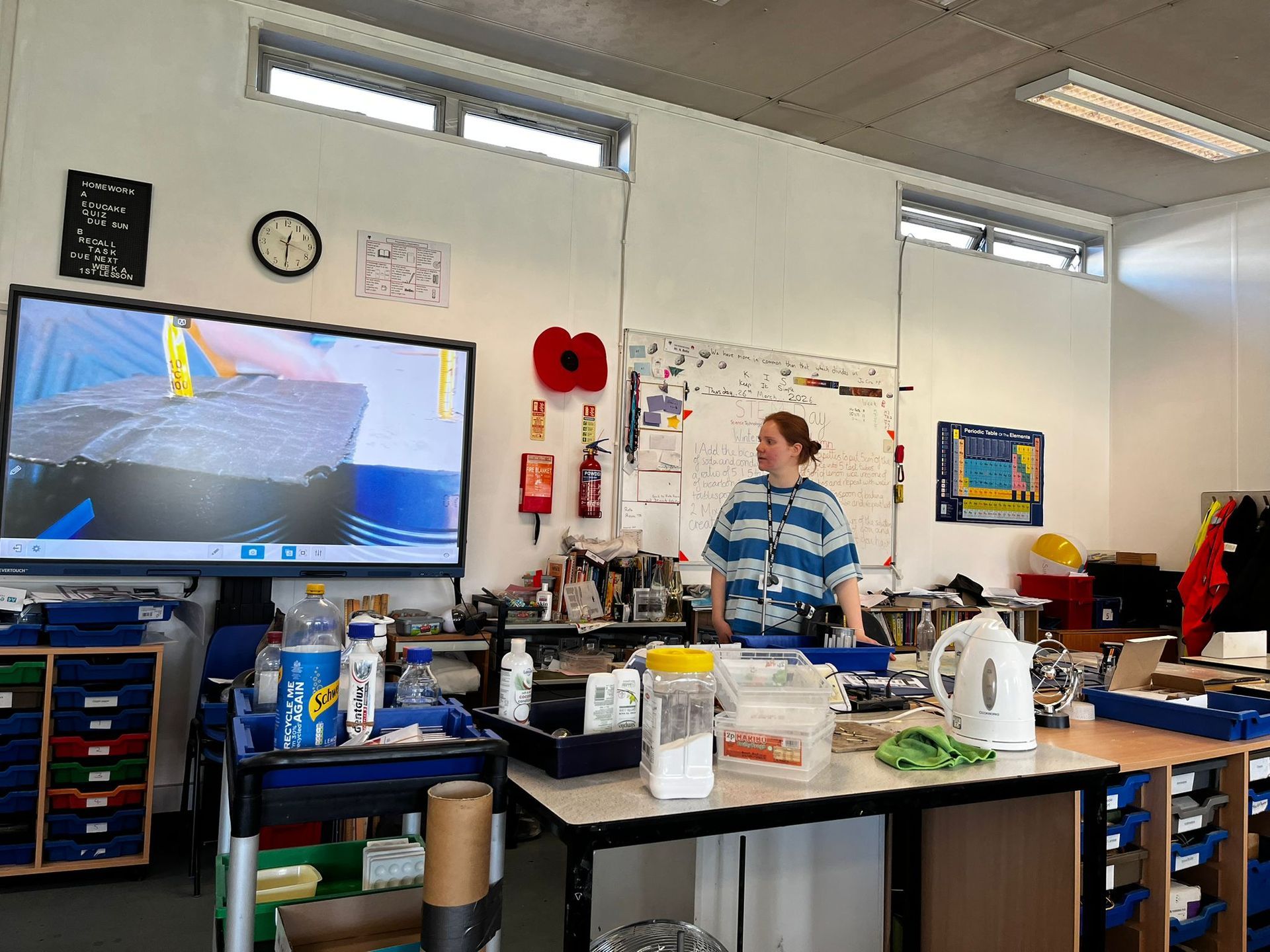 Workroom with a masked person in a blue striped shirt standing behind a cluttered lab bench.
