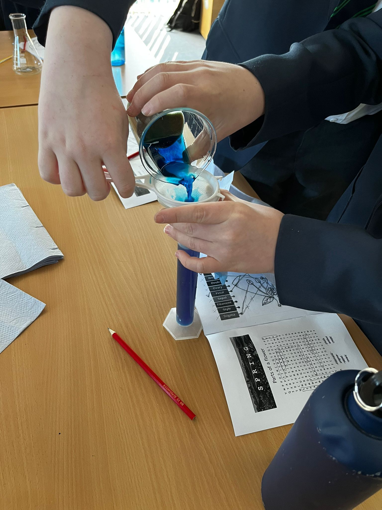 Hands assembling a blue-lit device over a wooden table with tools and papers nearby