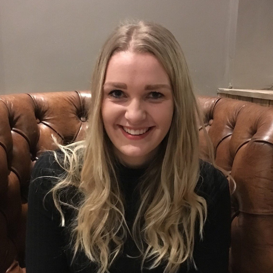 Smiling blonde woman in a black top seated on a brown leather couch
