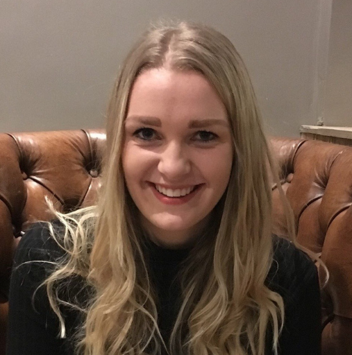Smiling blonde woman seated on a brown tufted leather chair against a gray wall.
