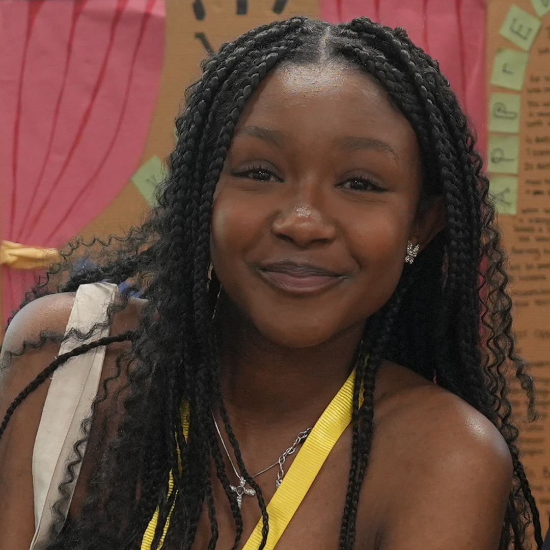 Smiling woman with long braids and a yellow strap in a pink indoor setting