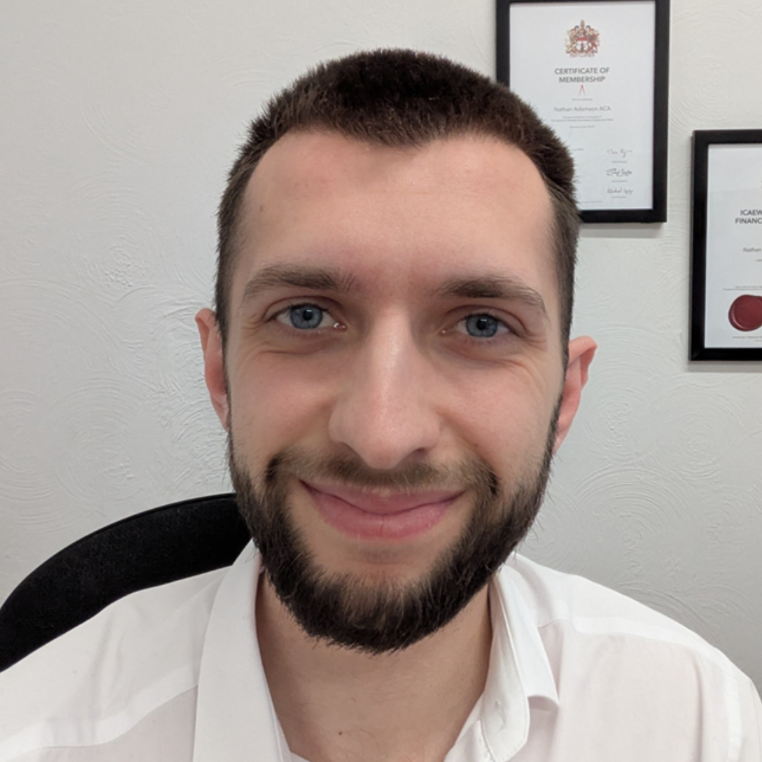 Smiling person in a white shirt seated indoors, with framed certificates on the wall behind.