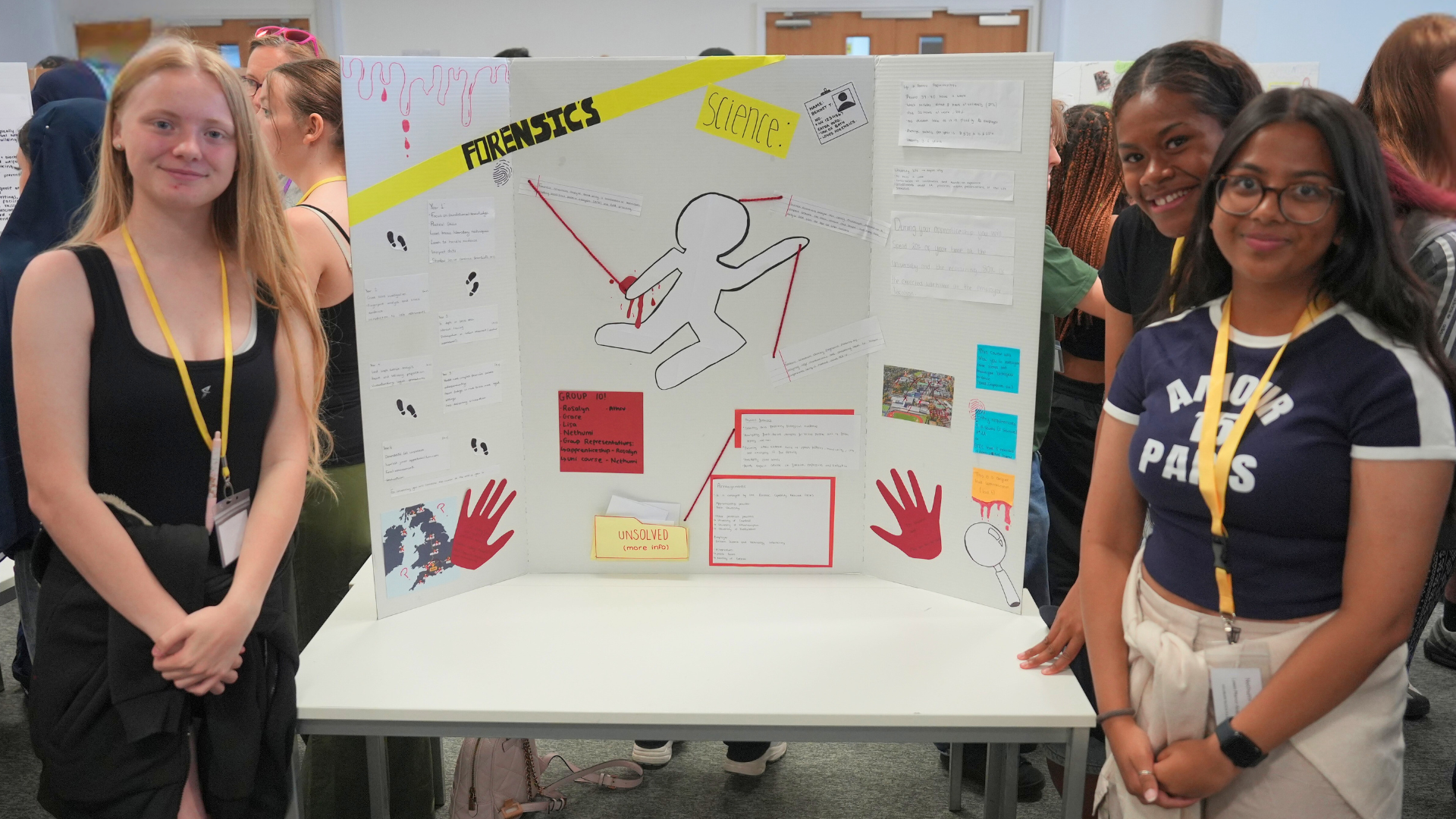 Three students posing beside a science fair poster board with diagrams, notes, and colorful sticky notes