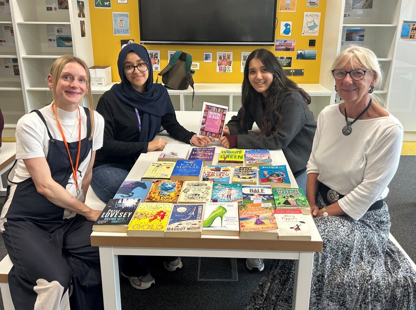 Four people seated around a table displaying colorful books in a classroom.