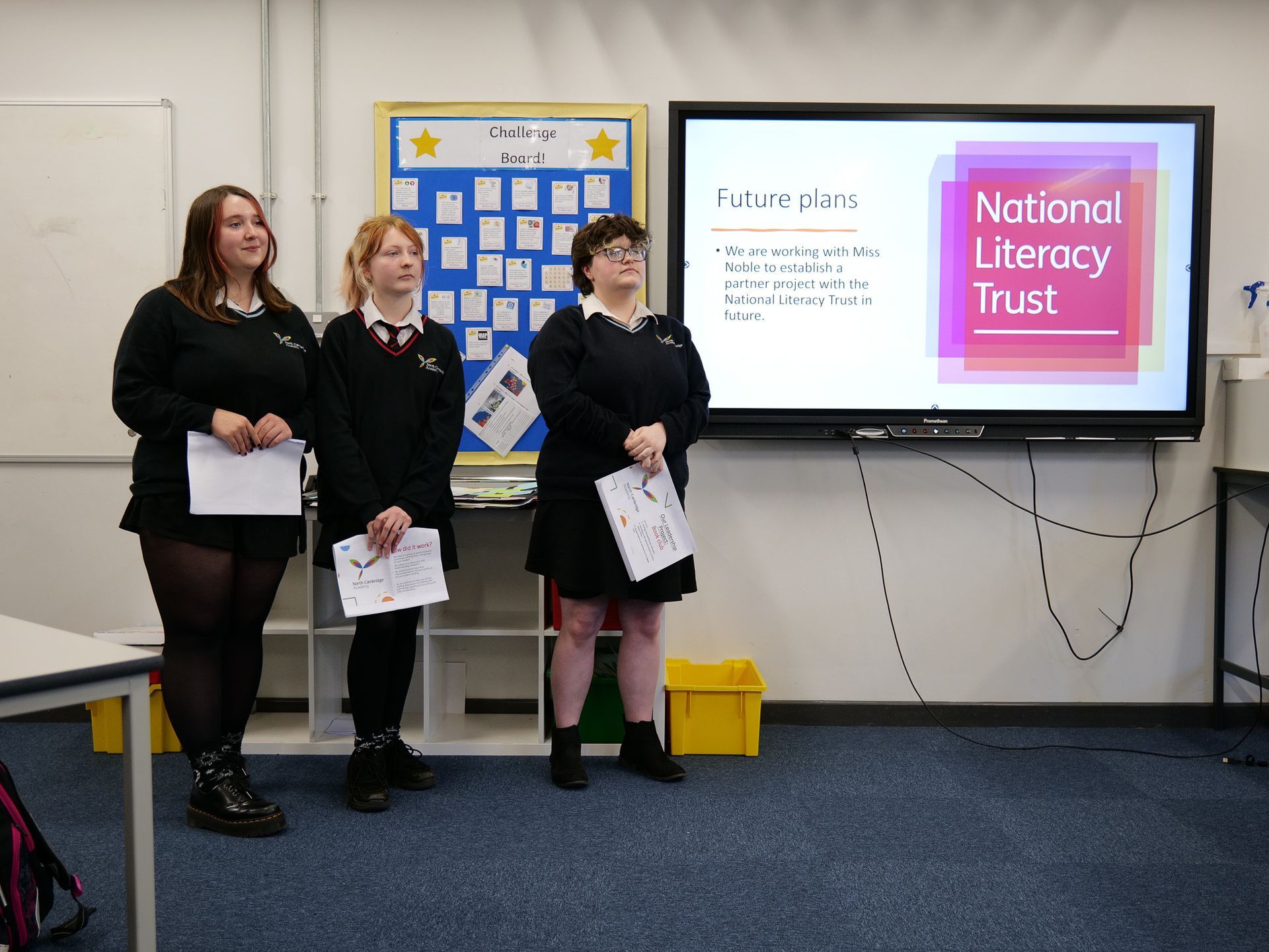 Three people standing beside a screen showing the National Literacy Trust logo in a classroom.