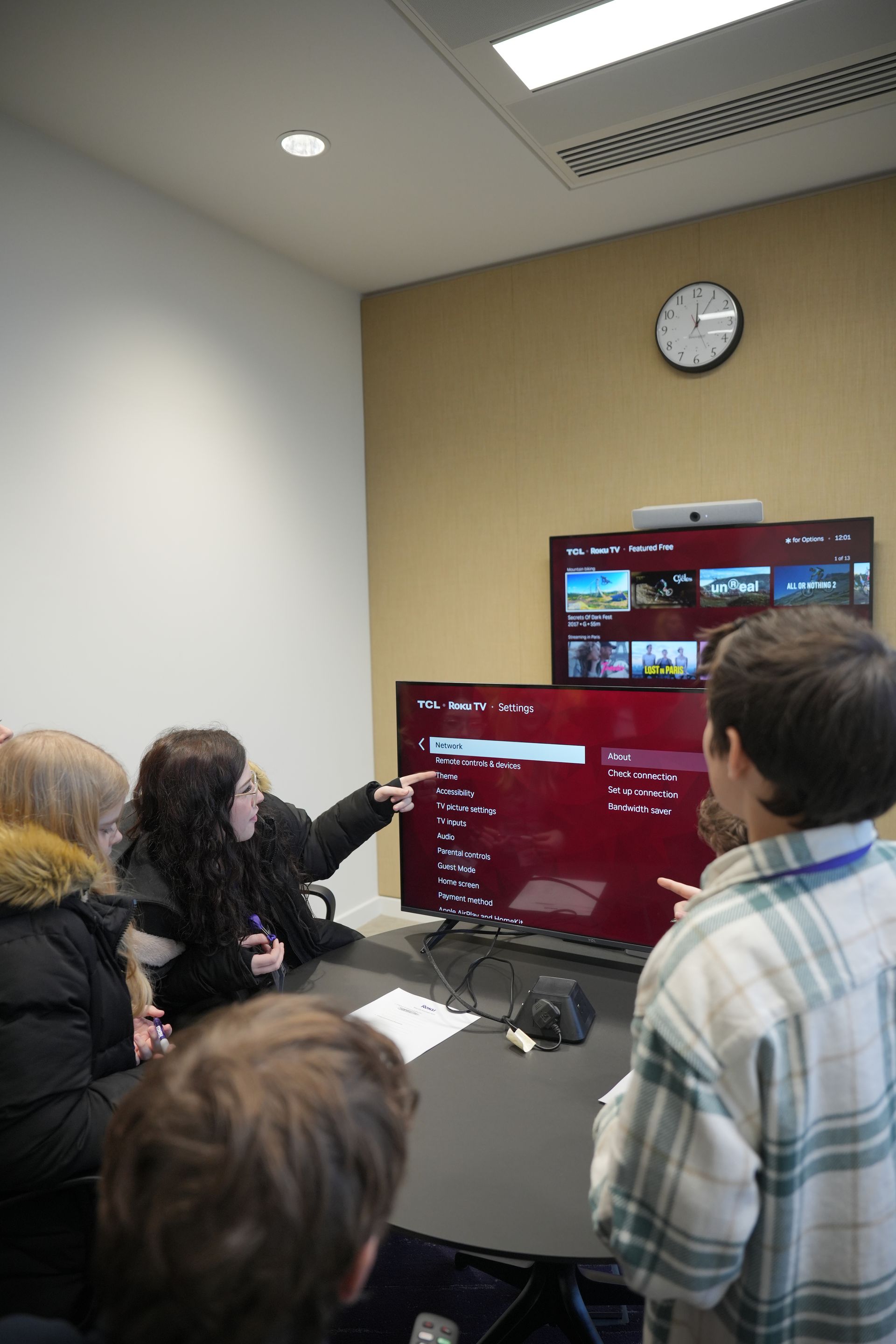A group of people are sitting around a table looking at a television.