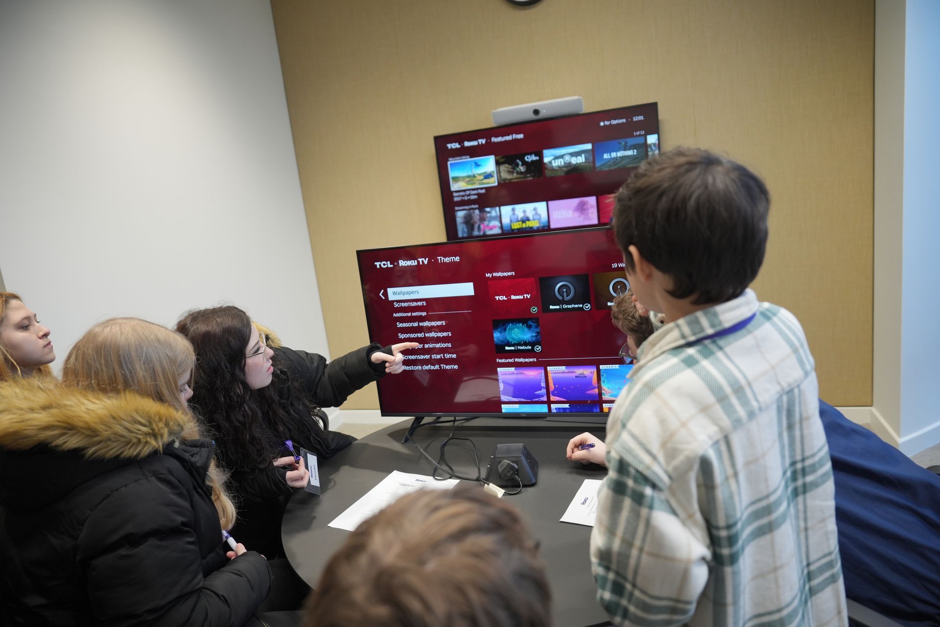 People gathered around a large TV, pointing at a red game or presentation screen in a meeting room.