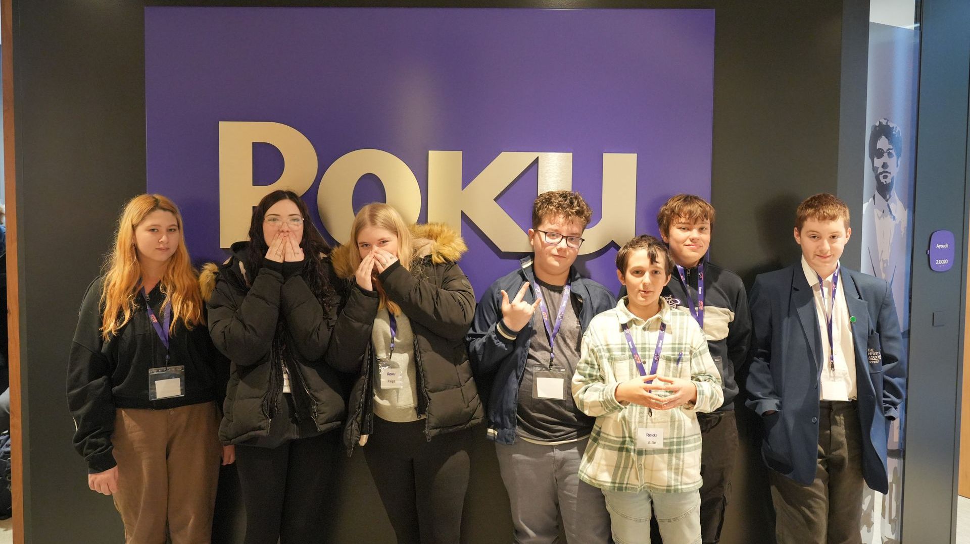 A group of young people are standing in front of a roku sign.
